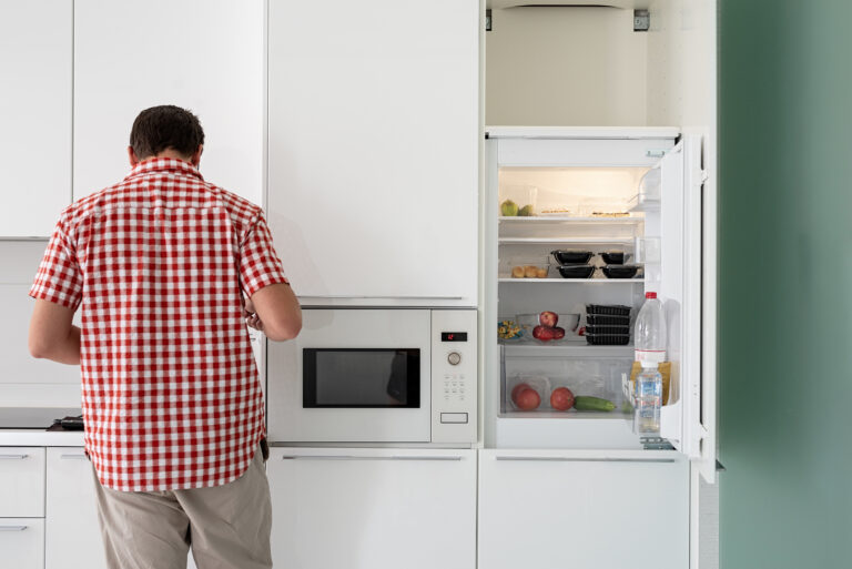 Young Man Makind Tea Standing Next To The Open Fridge.