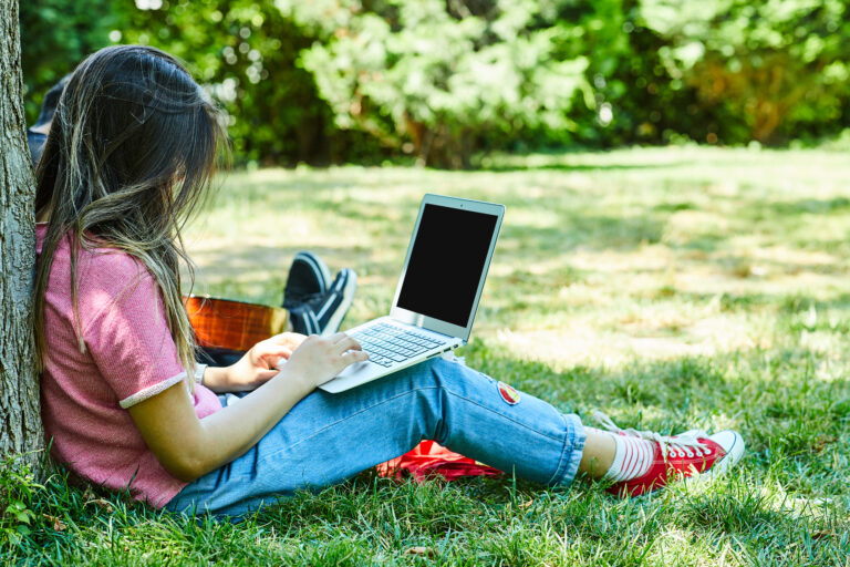 Young Woman Sitting On Green Grass While Using Laptop